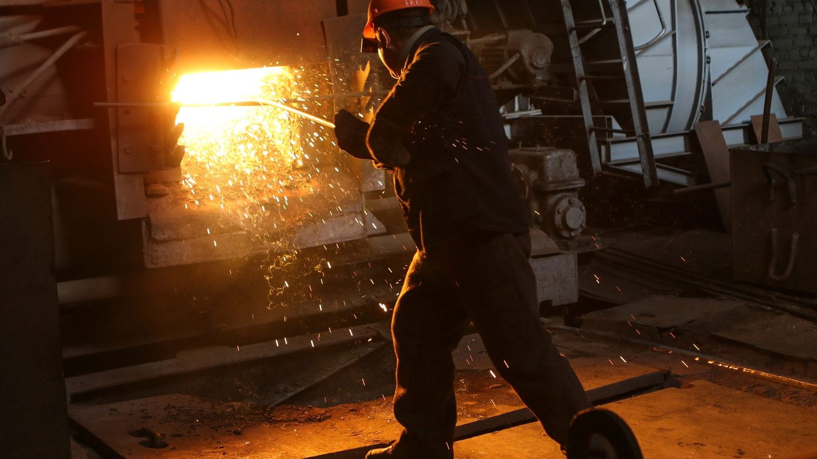 Arbeiter mit Schutzhelm an einem glühenden Industrieofen, Funken fliegen