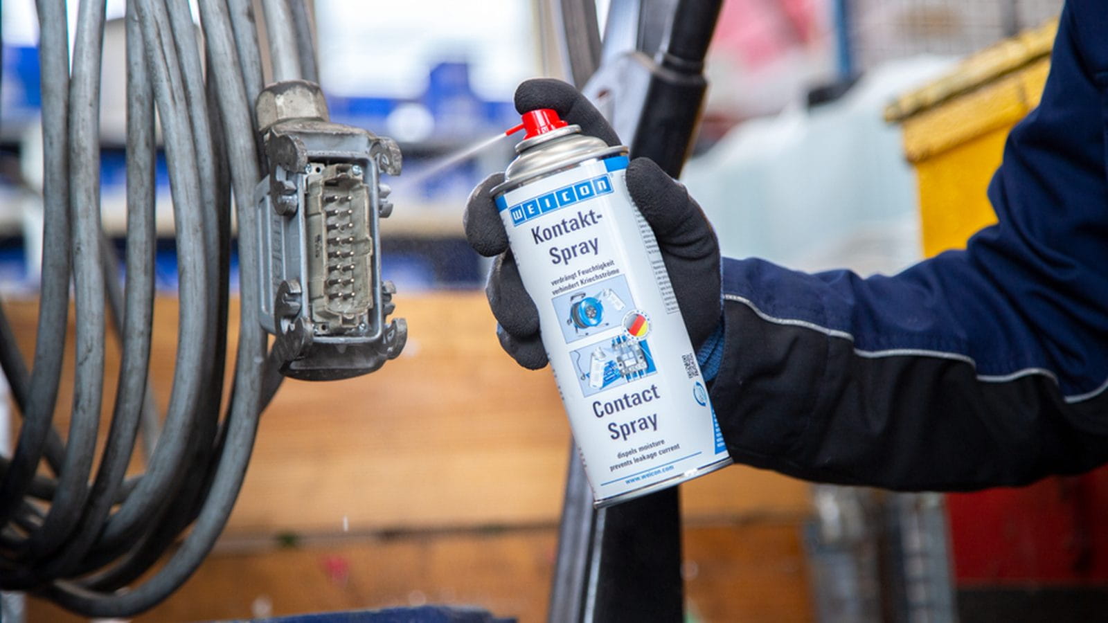 Kontaktspray wird auf einen mehrpoligen Industriesteckverbinder an einem Kabelbündel gesprüht