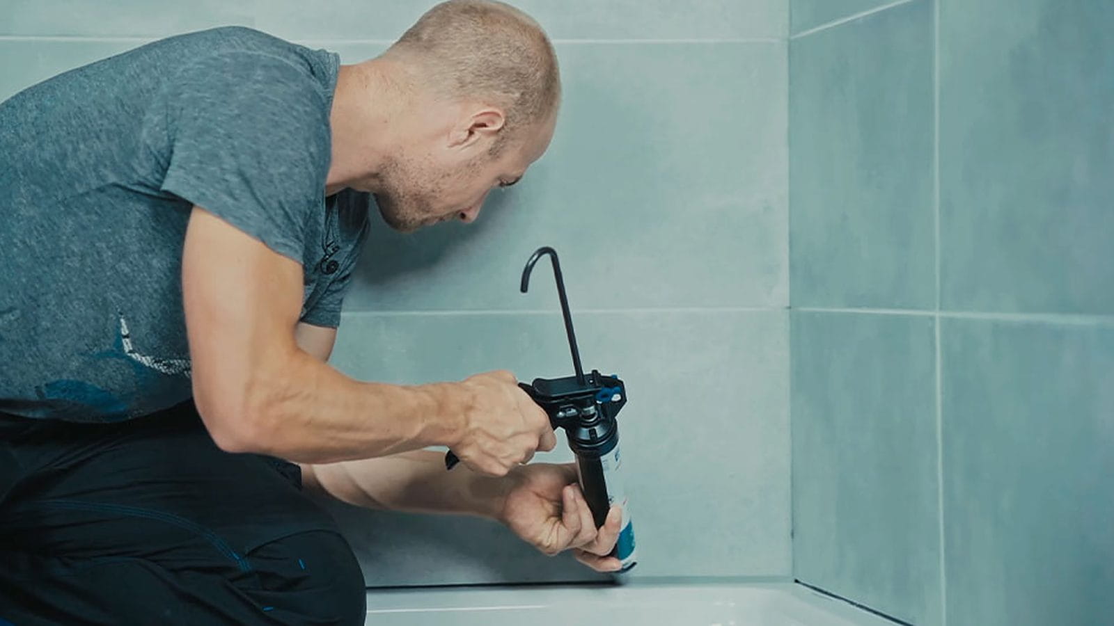 Handwerker spritzt mit der Kartuschenpistole Dichtstoff in die Fuge zwischen Duschwanne und Fliesenwand