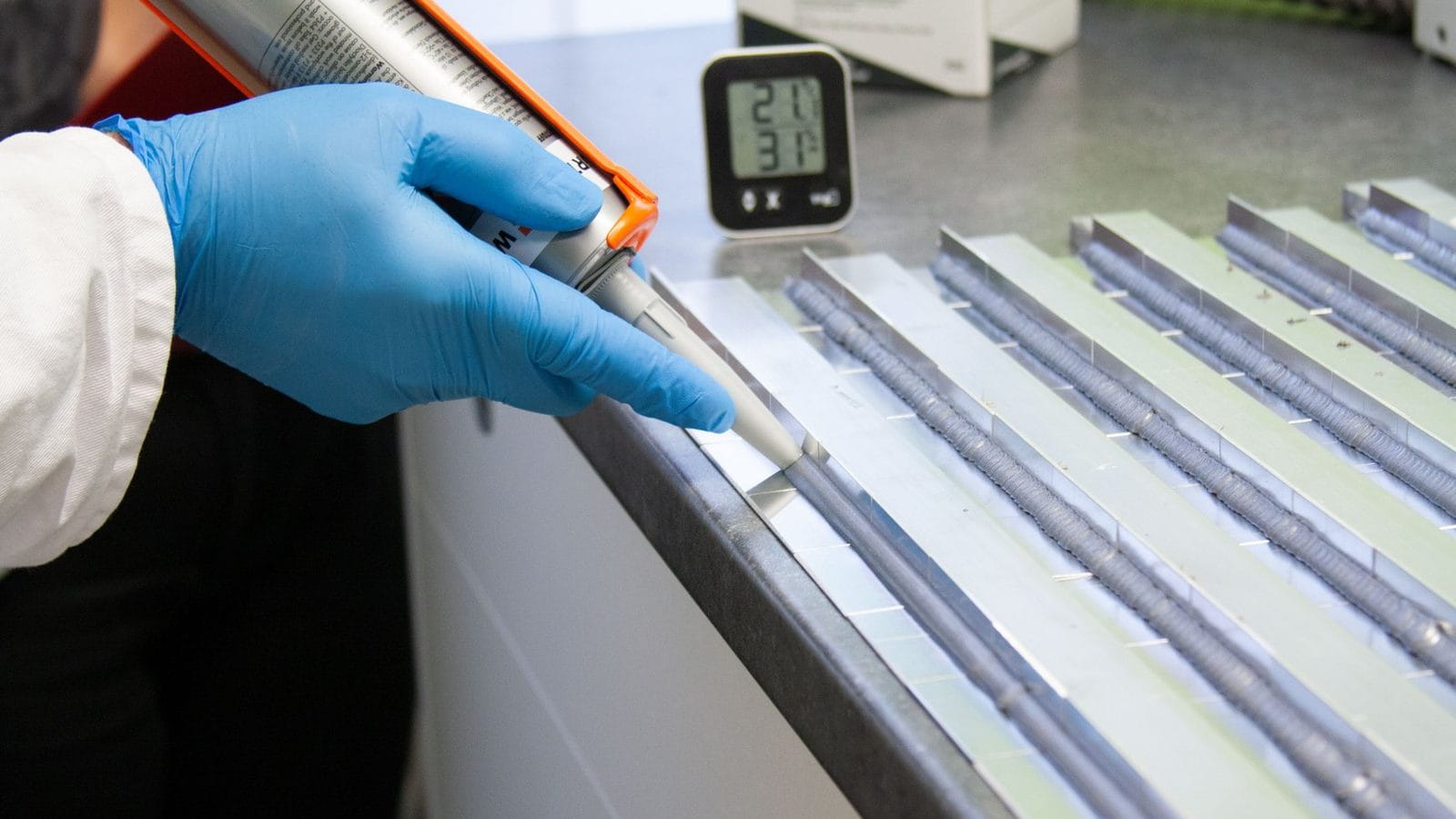 Klebstoffraupe wird mit der Kartusche auf Aluminiumprofile aufgetragen
